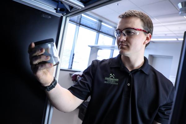 Student wearing safety glasses holding a jar in a mechanical engineering lab